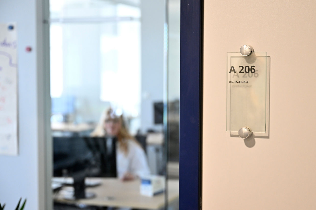 Eingangstür Digitalfiliale mit einer Mitarbeiterin im Hintergrund, die am Schreibtisch sitzt