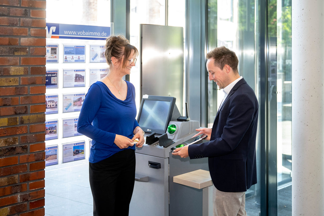Ein Berater erklärt der Kundin etwas vor dem Überweisungsterminal