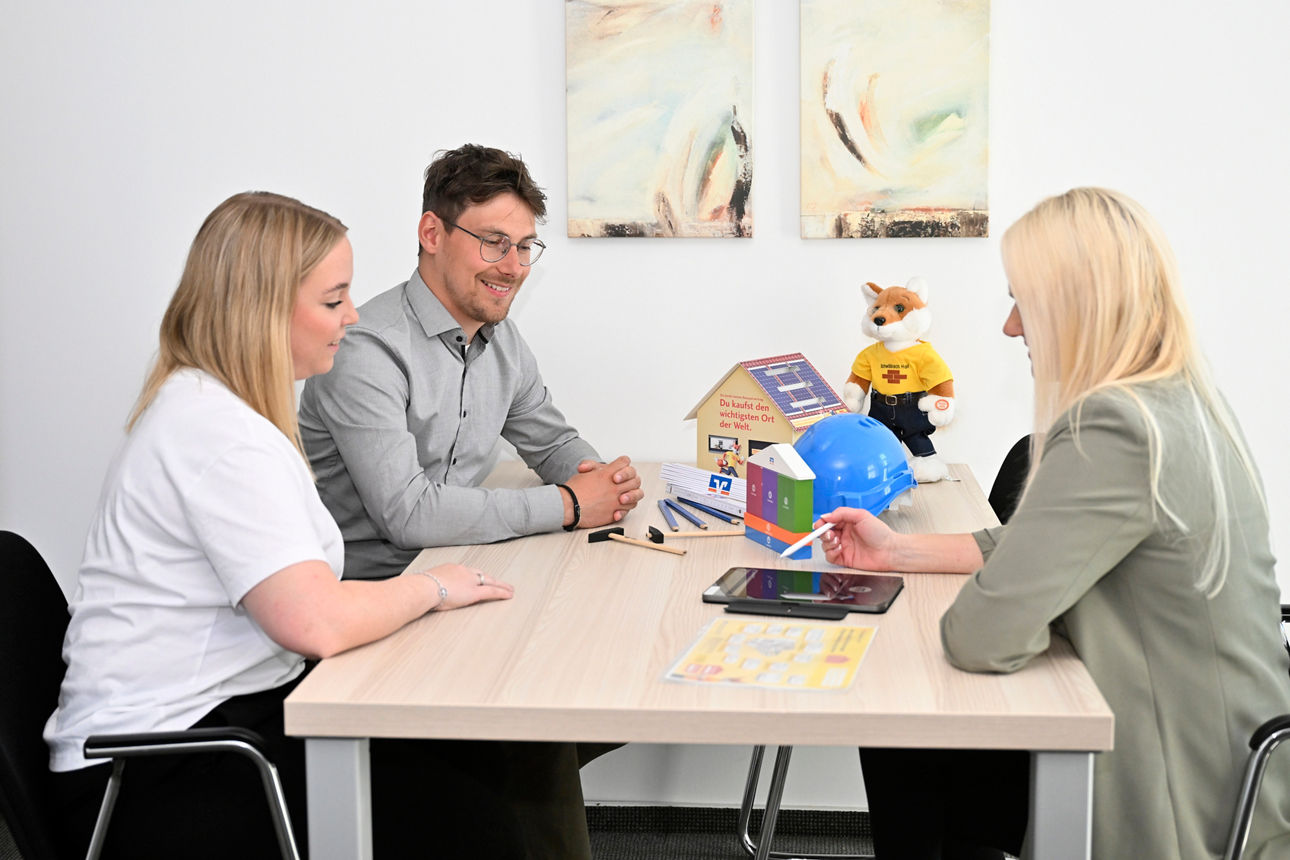 Kunden sitzen mit der Beraterin am Tisch für ein Baufi Gespräch