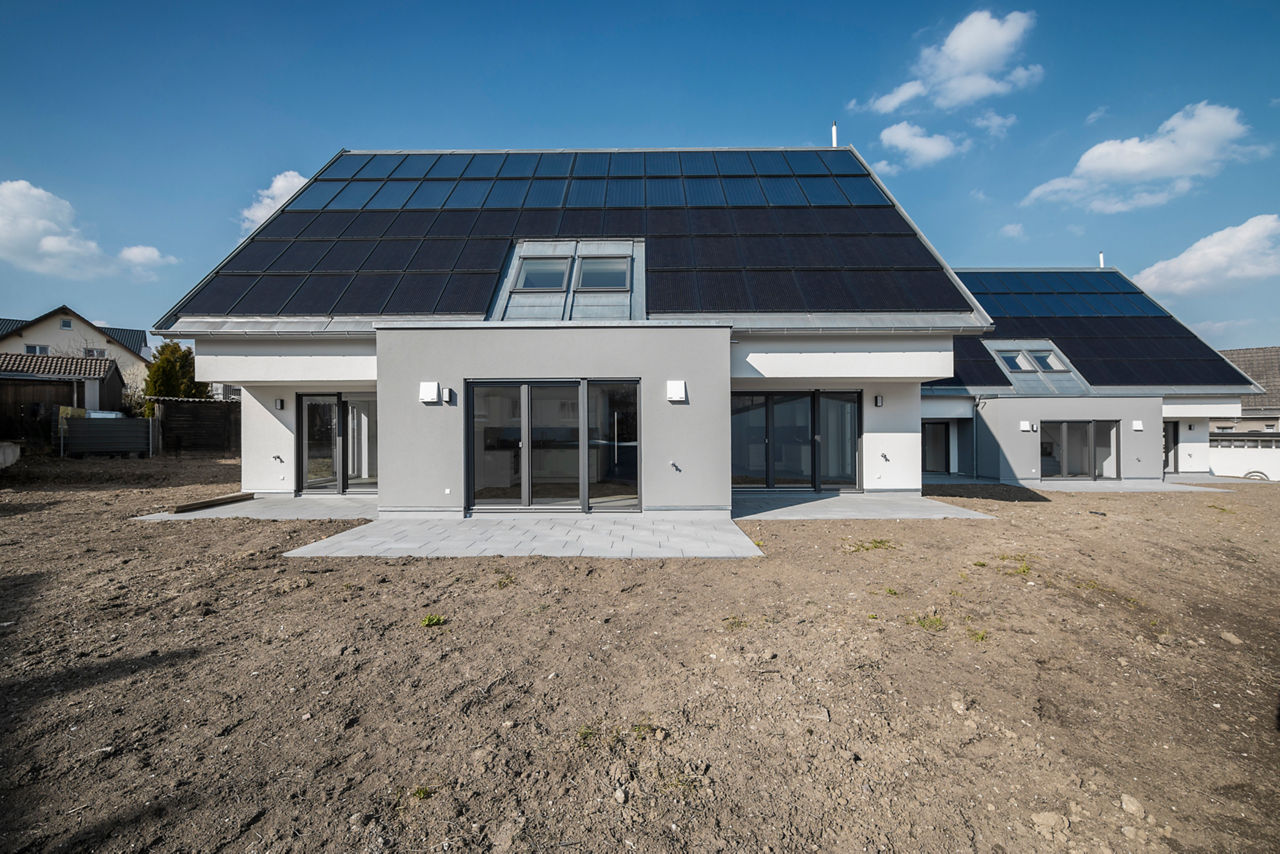 Zwei moderne Mehrfamilienhäuser mit heller Fassade und großen Fenstern stehen nebeneinander. Auf den Dächern sind Solarpaneele installiert. 