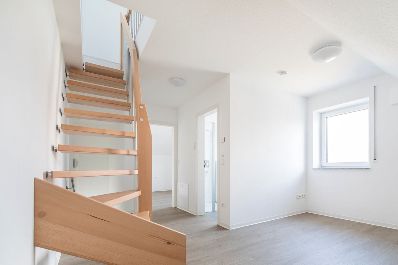 Darstellung des Windfangs eines modernen, energieautarken Mehrfamilienhauses. Auf der linken Seite ist eine Holztreppe zu sehen, welche ins OG führt. 