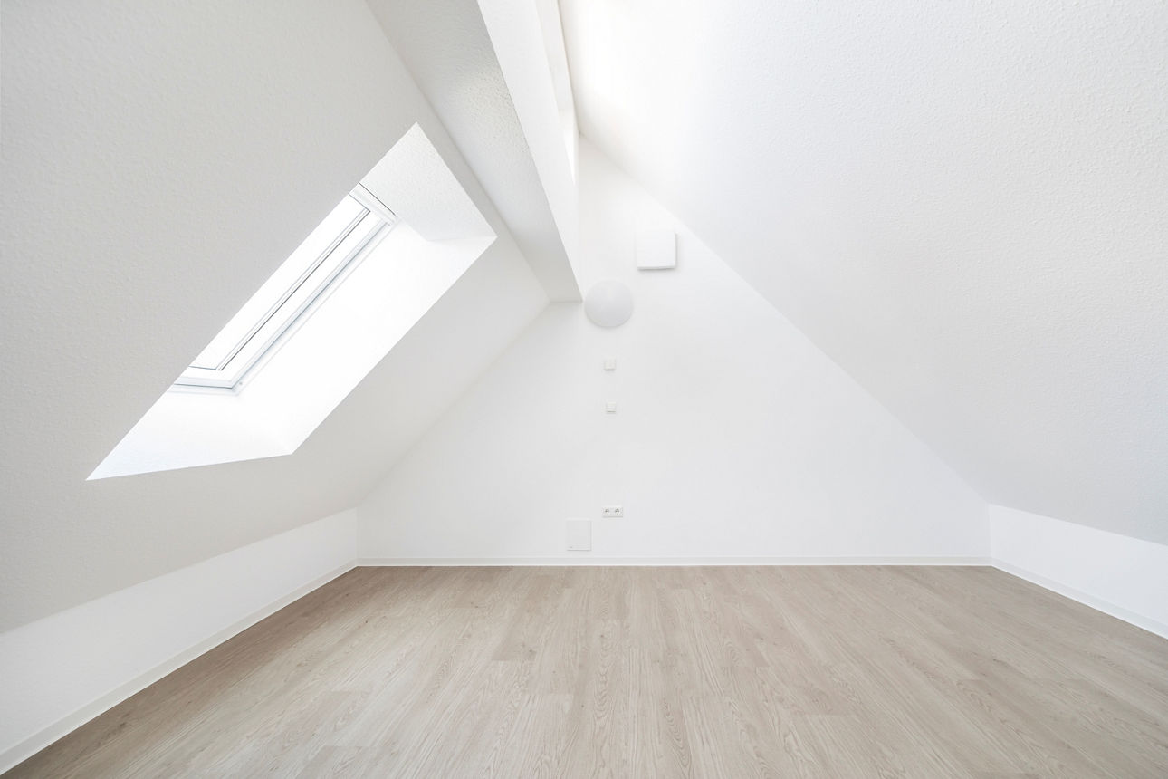 Darstellung der Galerie im Dachspitz eines modernen, energieautarken Mehrfamilienhauses. Auf der linken Seite befindet sich ein großes Dachfenster. Rechts und links sind Dachschrägen zu erkennen. 