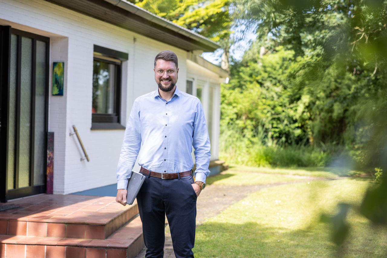 Mann steht vor einem Haus und hält einen Laptop unter dem Arm.