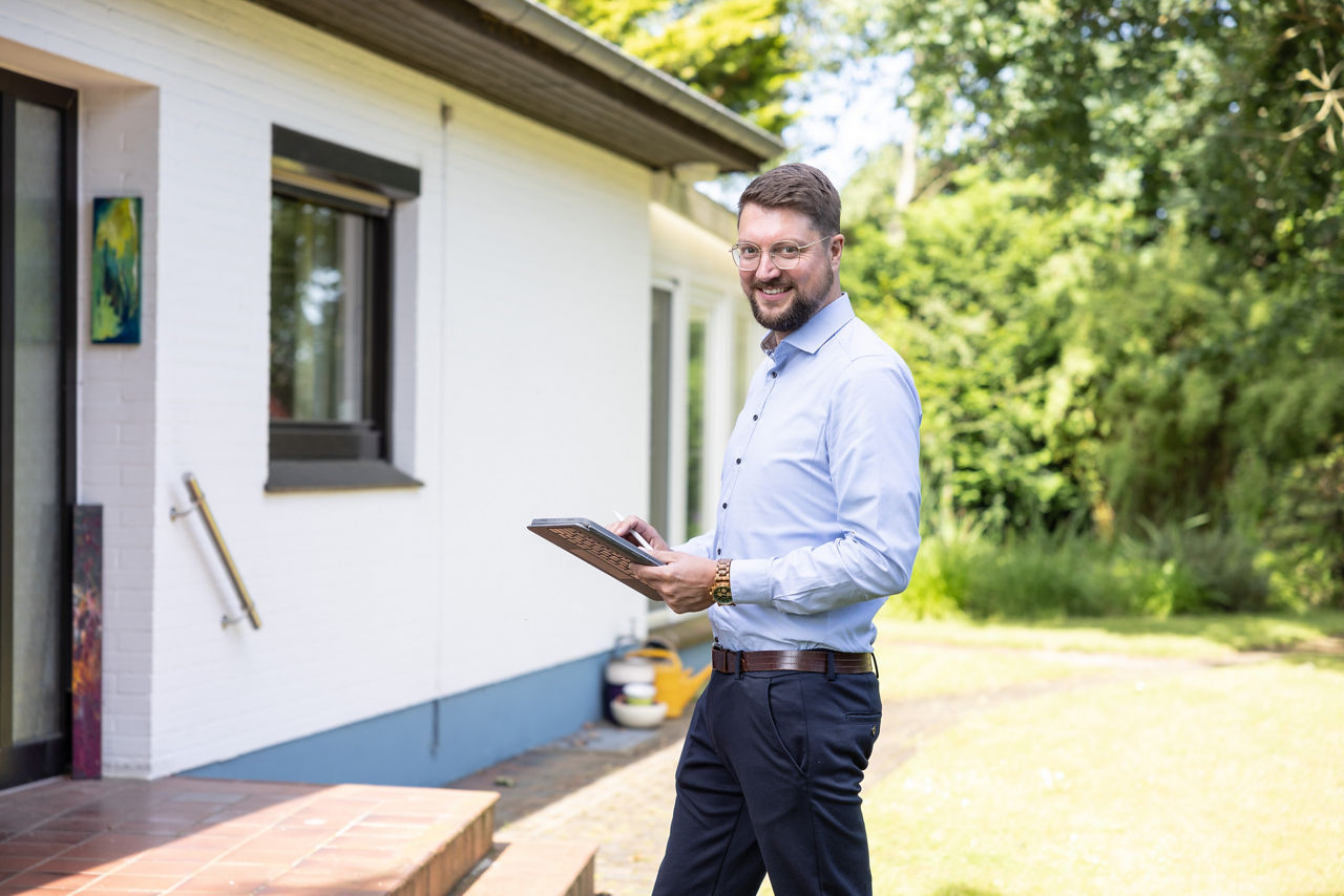 Immobilien Makler steht im Garten vor Haus