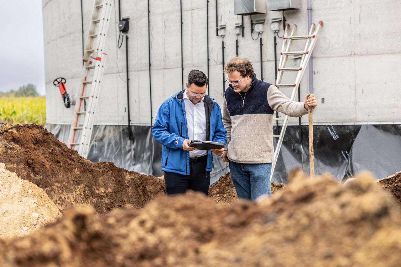 Zwei Männer stehen vor einer landwirtschaftlichen Anlage.