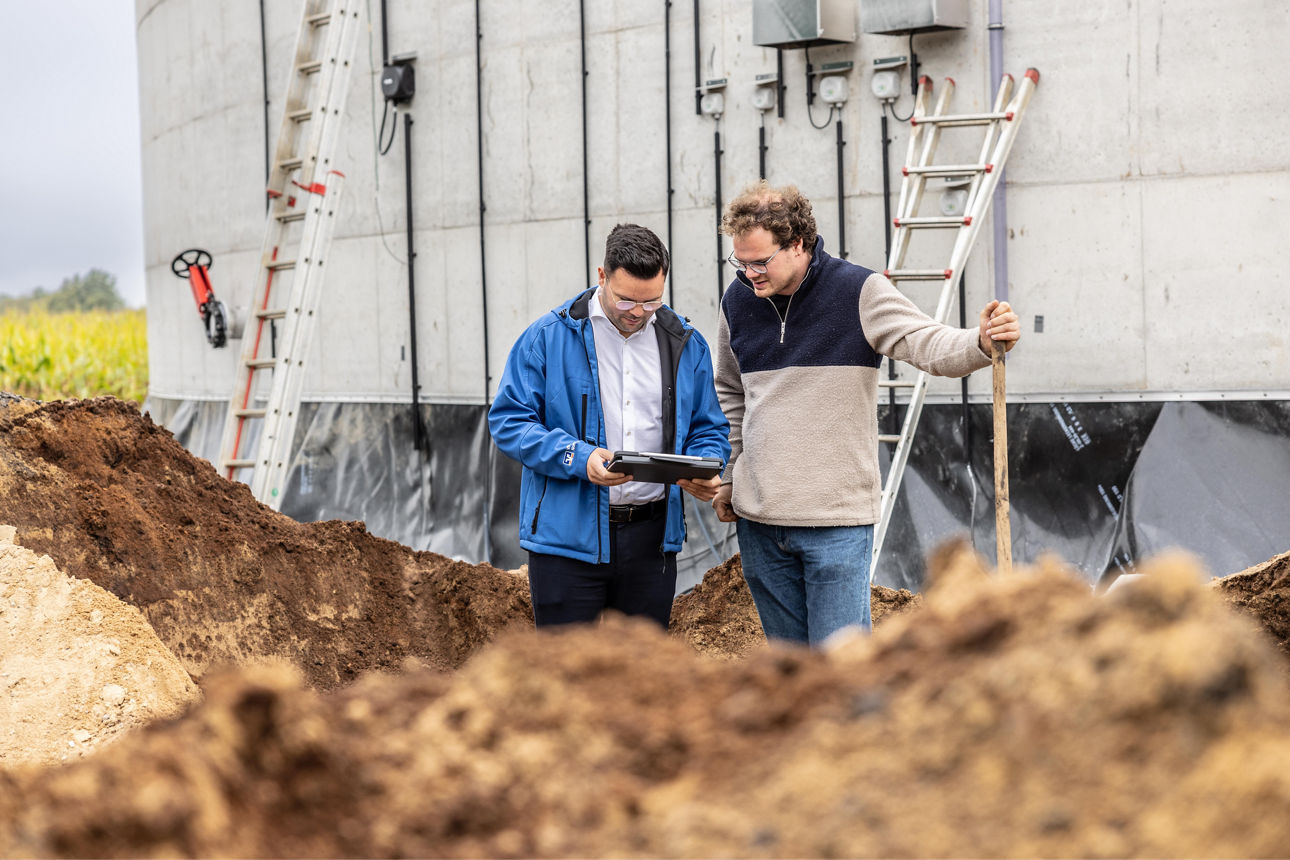Zwei Männer stehen vor einer landwirtschaftlichen Anlage.