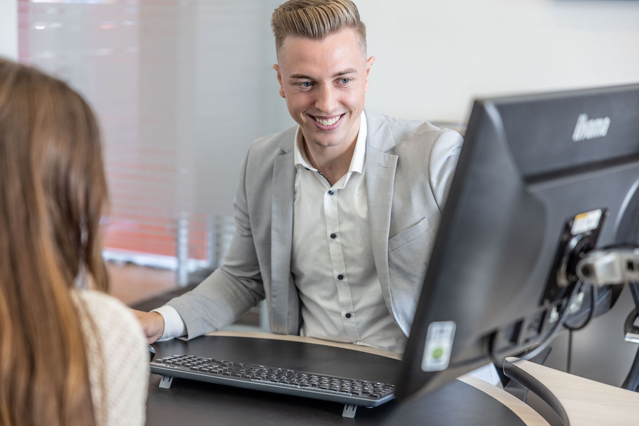 Kundenberater berät eine Kundin und zeigt auf einem Monitor