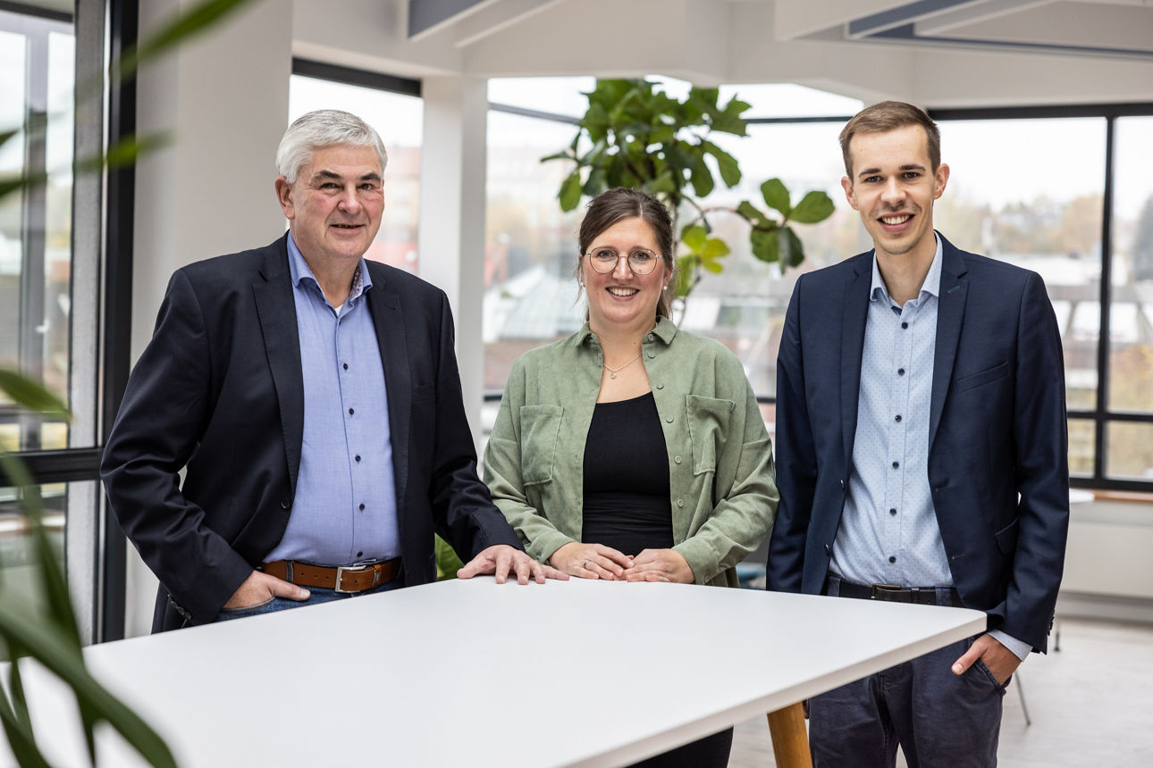 Drei Personen stehen an einem weißen Tisch in einem modernen Büro.