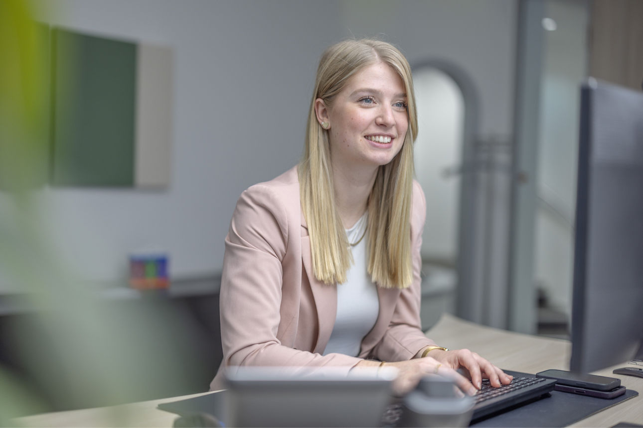 Eine junge Frau sitzt an einem Schreibtisch und arbeitet konzentriert am Computer.