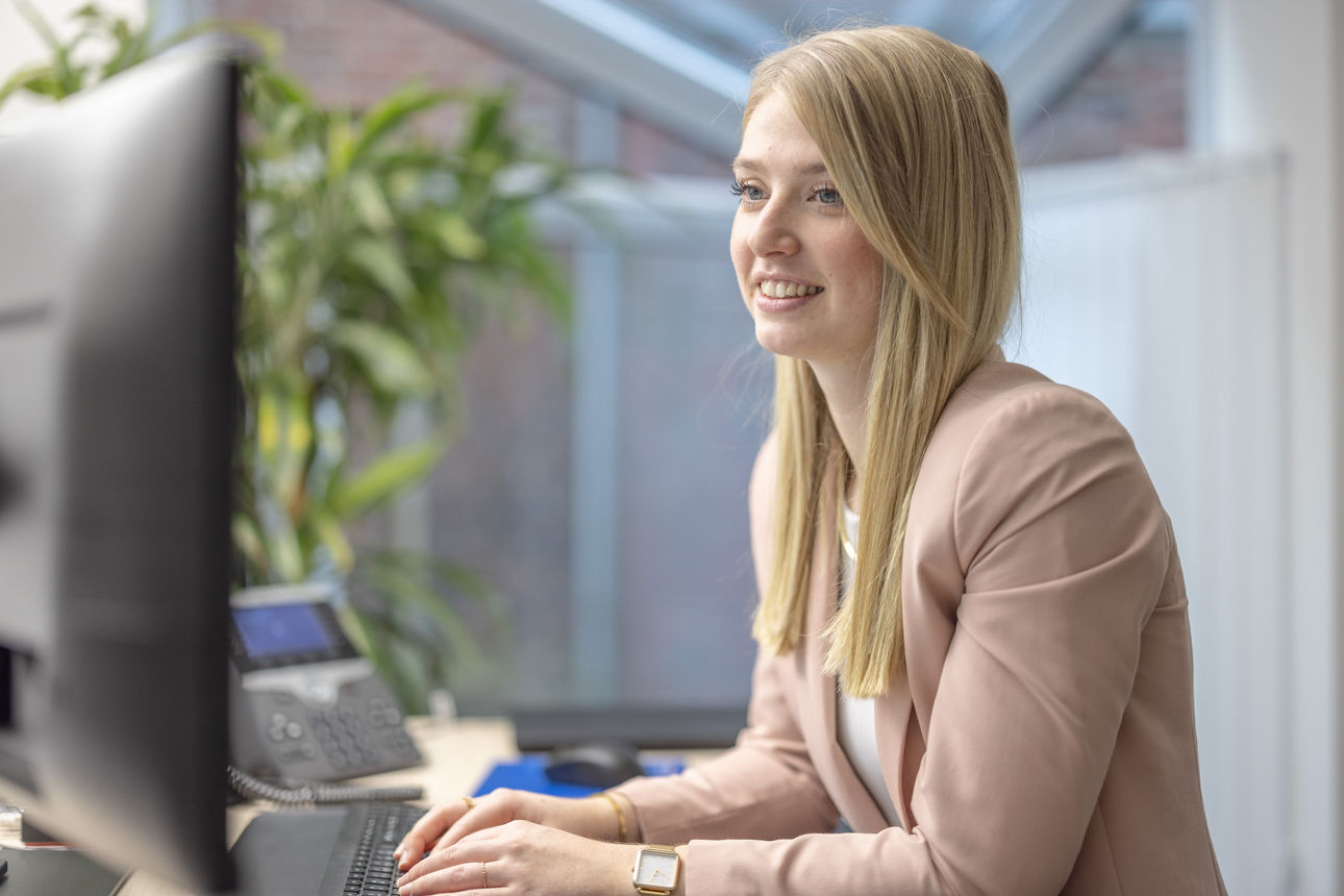 Eine junge Frau sitzt an einem Schreibtisch und arbeitet konzentriert am Computer.