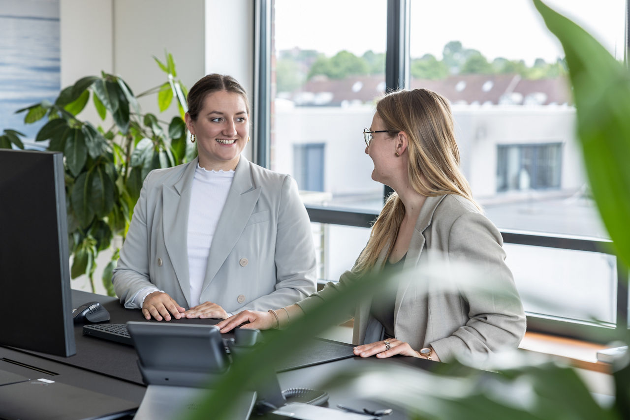 Zwei Frauen stehen an einem Schreibtisch und unterhalten sich.