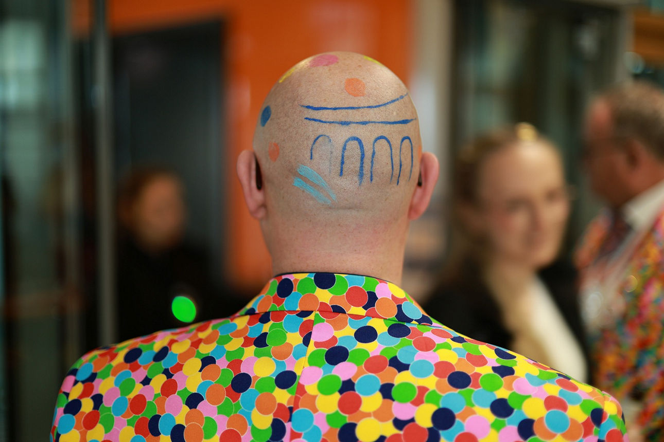 Mann mit kahlem Hinterkopf hat eine Konfetti-Bemalung und das Raiba-Logo geschminkt