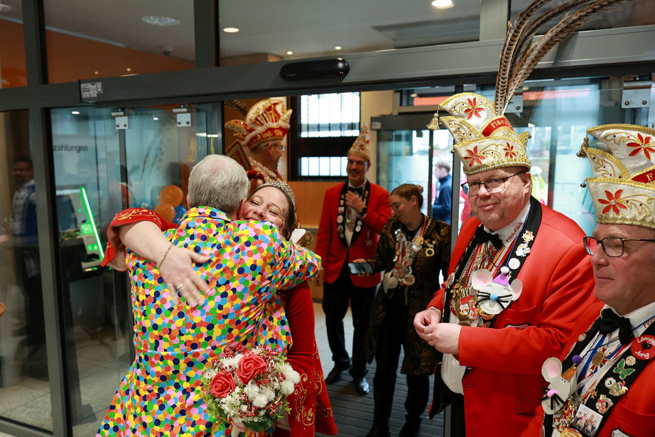 Vorstand Konrad Breul im Konfetti-Kostüm begrüßt die Asbacher Prinzessin im rot-weißen Kleid mit einer Umarmung