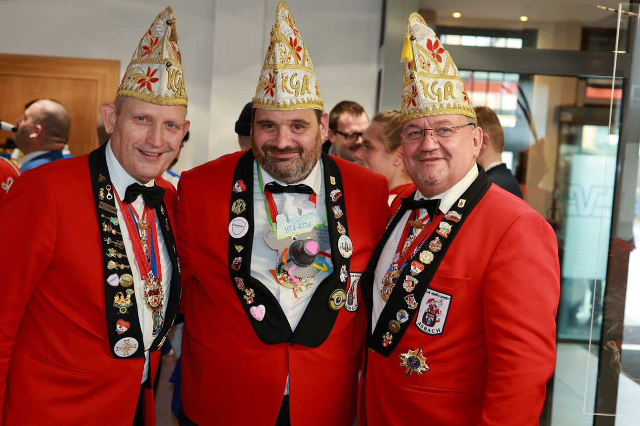 Drei Mitglieder des Club gemötlichkeit Asbach in rot-schwarzen Fracks und rot-goldenen Narrenkappen stehen nebeneinander