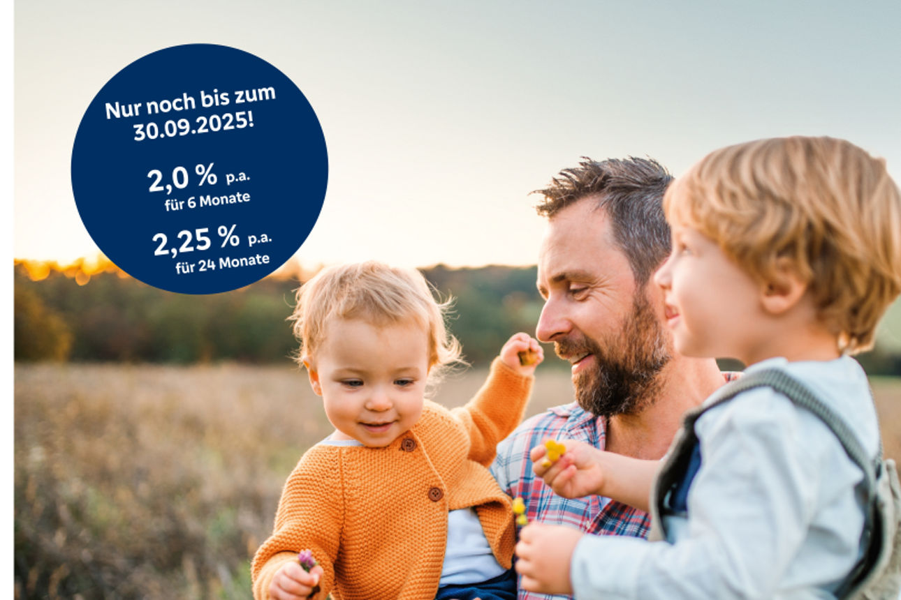 EIn Vater steht auf einem Feld und hat seine Kinder auf dem Arm