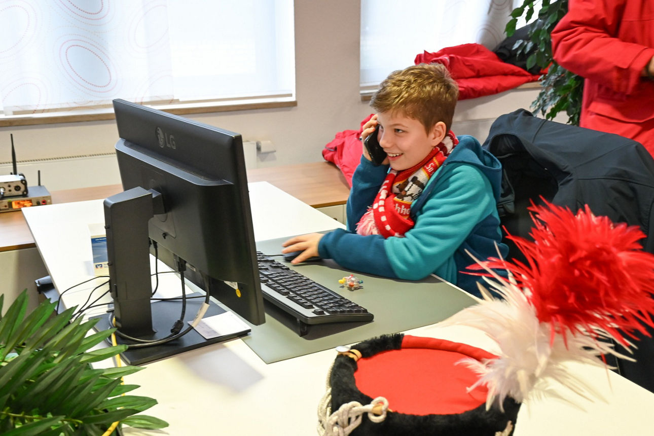 Ein Junge sitzt an einem Schreibtisch in der Geschäftsstelle, tippt auf der Tastatur und telefoniertDie KG Flöck Flöck Limach