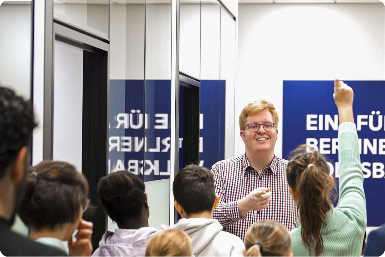 Ein Auszubildender der Berliner Volksbank steht vor Kindern und beantwortet Fragen