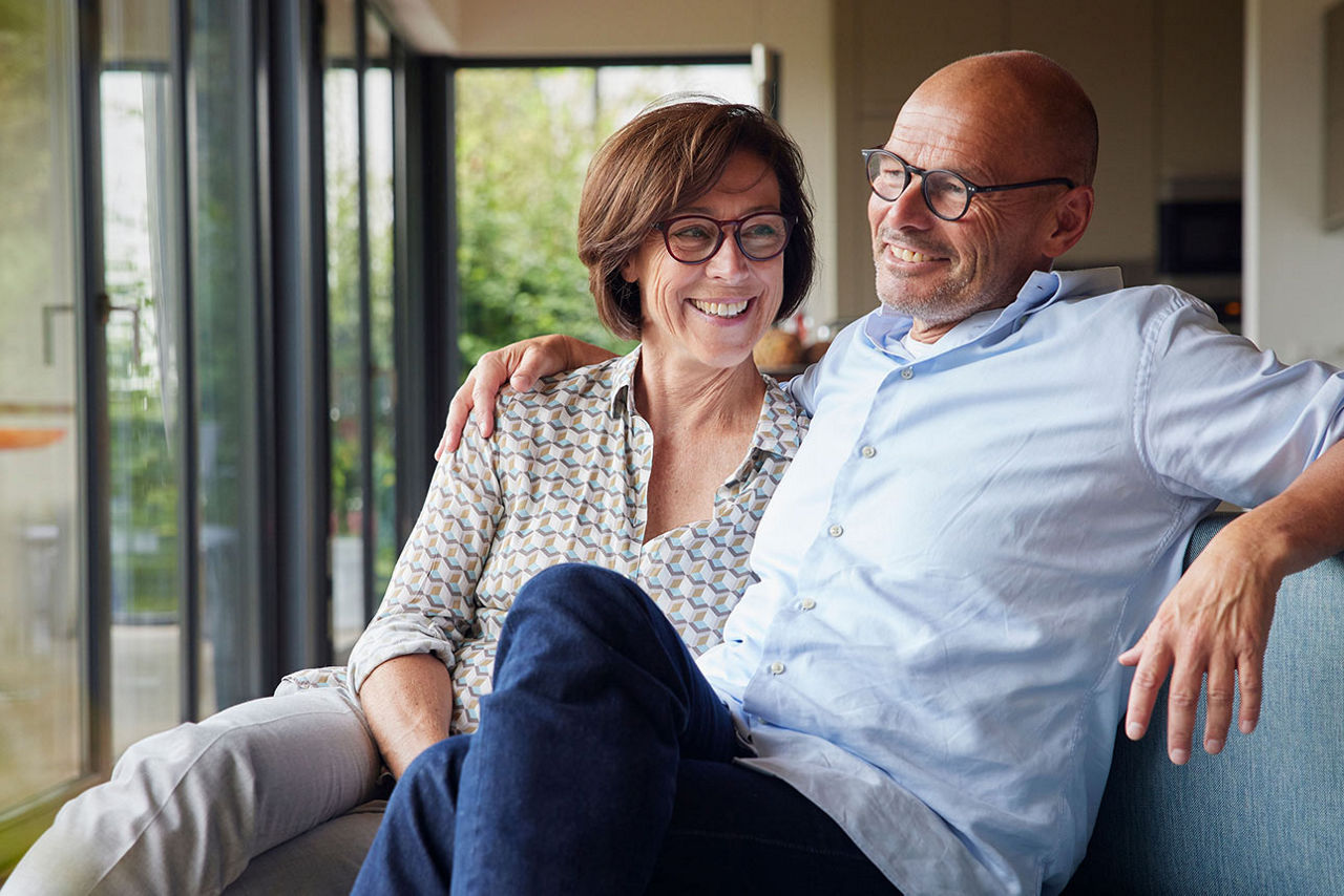 Mann und Frau sitzen lächelnd Arm in Arm auf einem Sofa