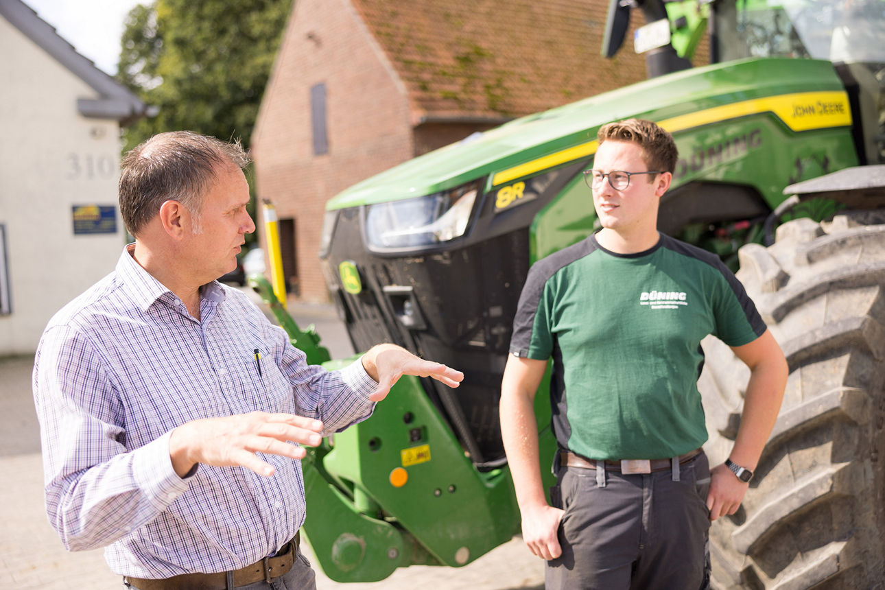 Agrarkundenberater Rainer Wiebke im Gespräch mit Geschäftsführer Fabian Düning, im Hintergrund eine Landmaschine.