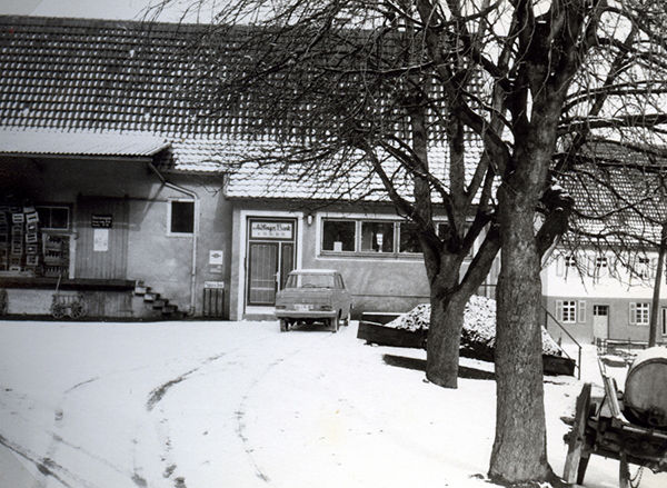 Schwarz-Weiß-Foto, das einen Hof, ein Auto, Schnee und ein Haus zeigt