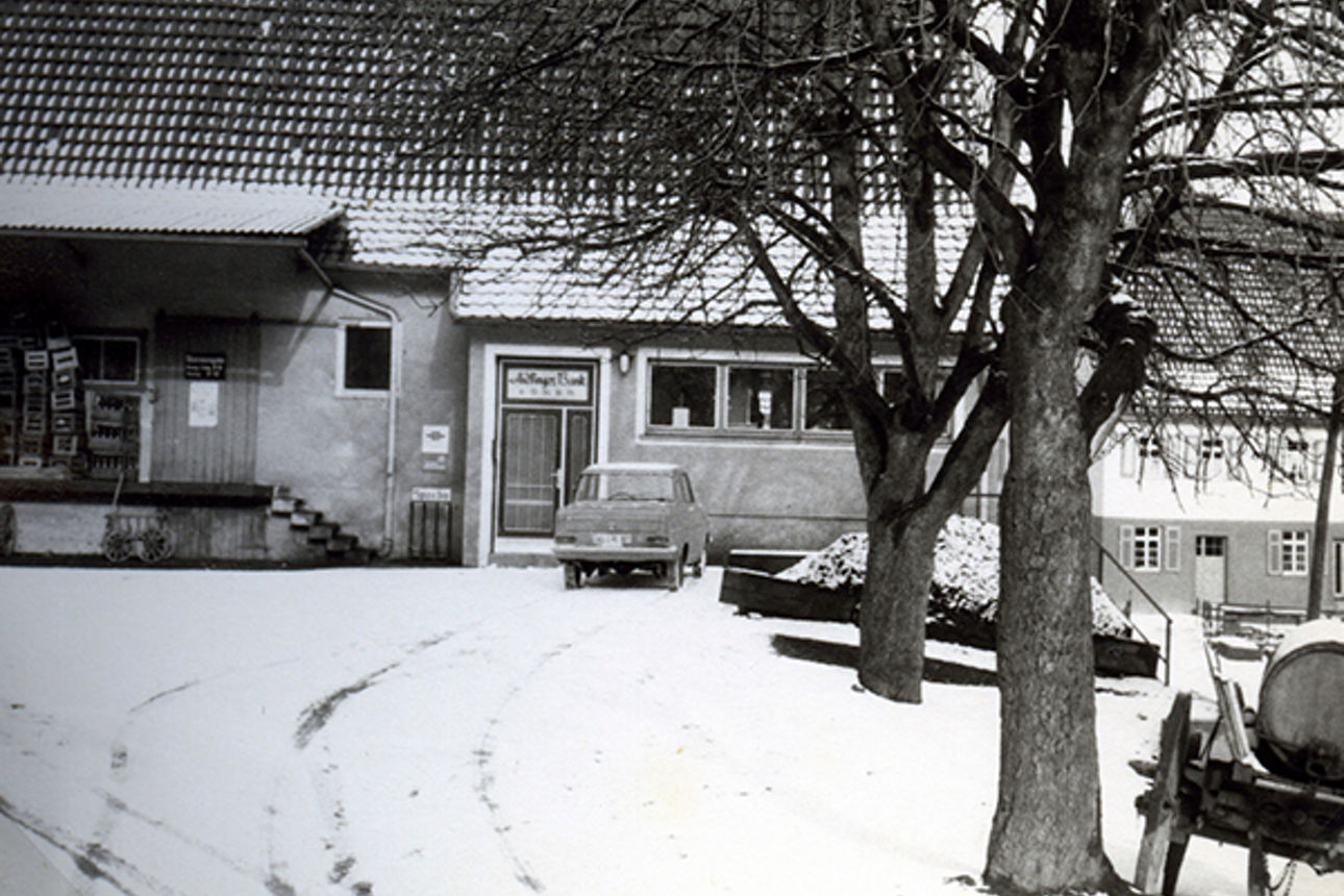 Schwarz-Weiß-Foto, das einen Hof, ein Auto, Schnee und ein Haus zeigt