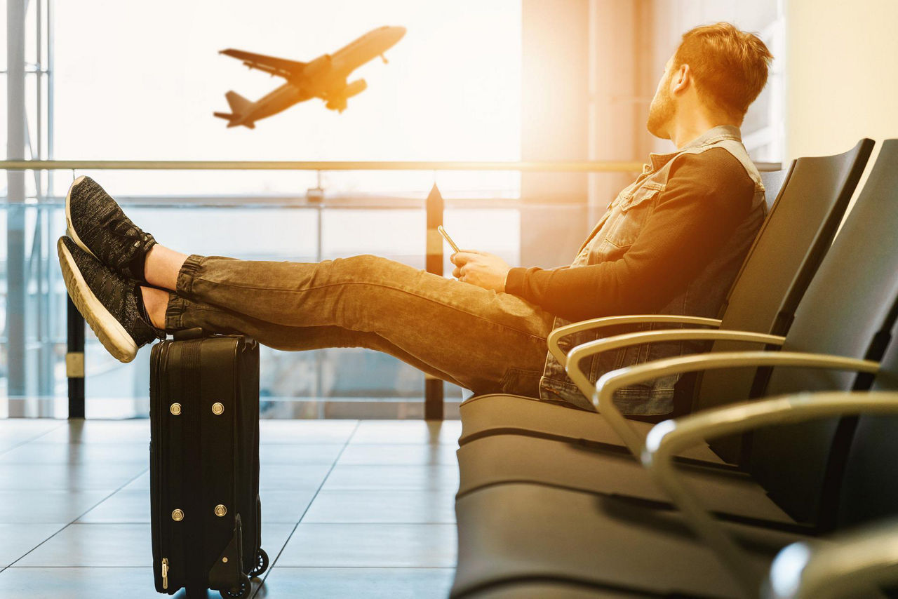 Am Gate wartender Fluggast beobachtet durchs Fenster ein Flugzeug beim Abflug