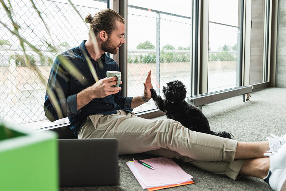 Ein Mann sitzt mit einer Tasse Kaffee auf dem Boden und gibt seinem Hund ein High Five