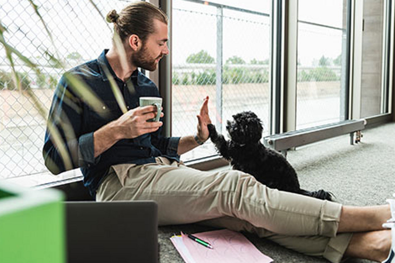 Ein Mann sitzt mit einer Tasse Kaffee auf dem Boden und gibt seinem Hund ein High Five
