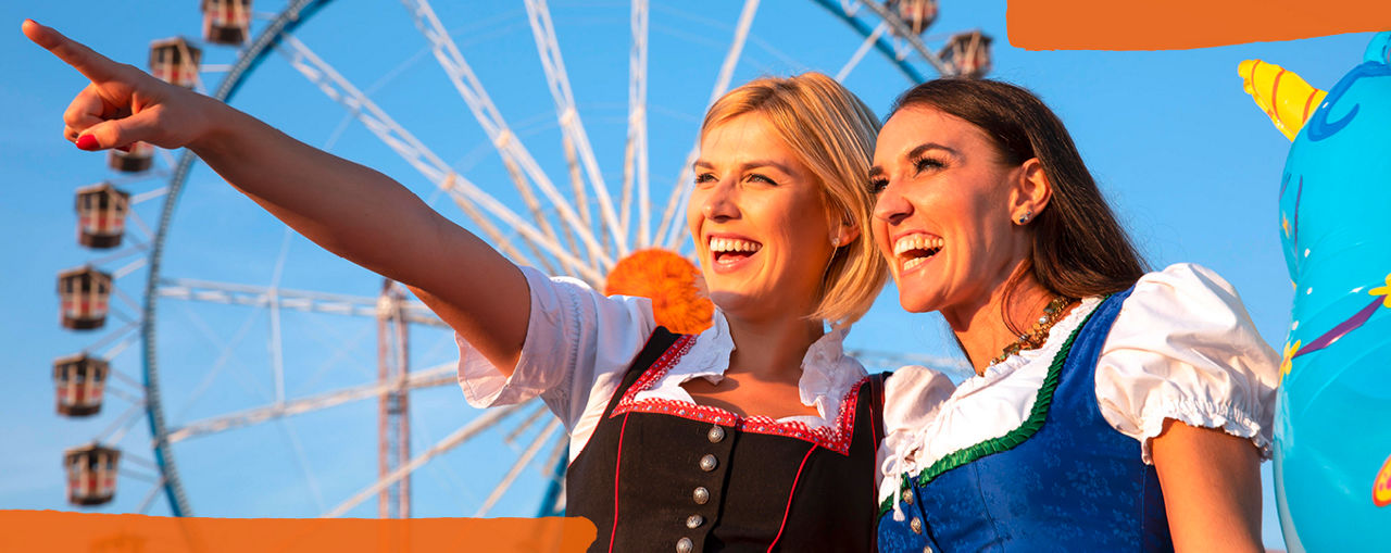 Zwei Frauen in Tracht stehen lächelnd vor einem Riesenrad