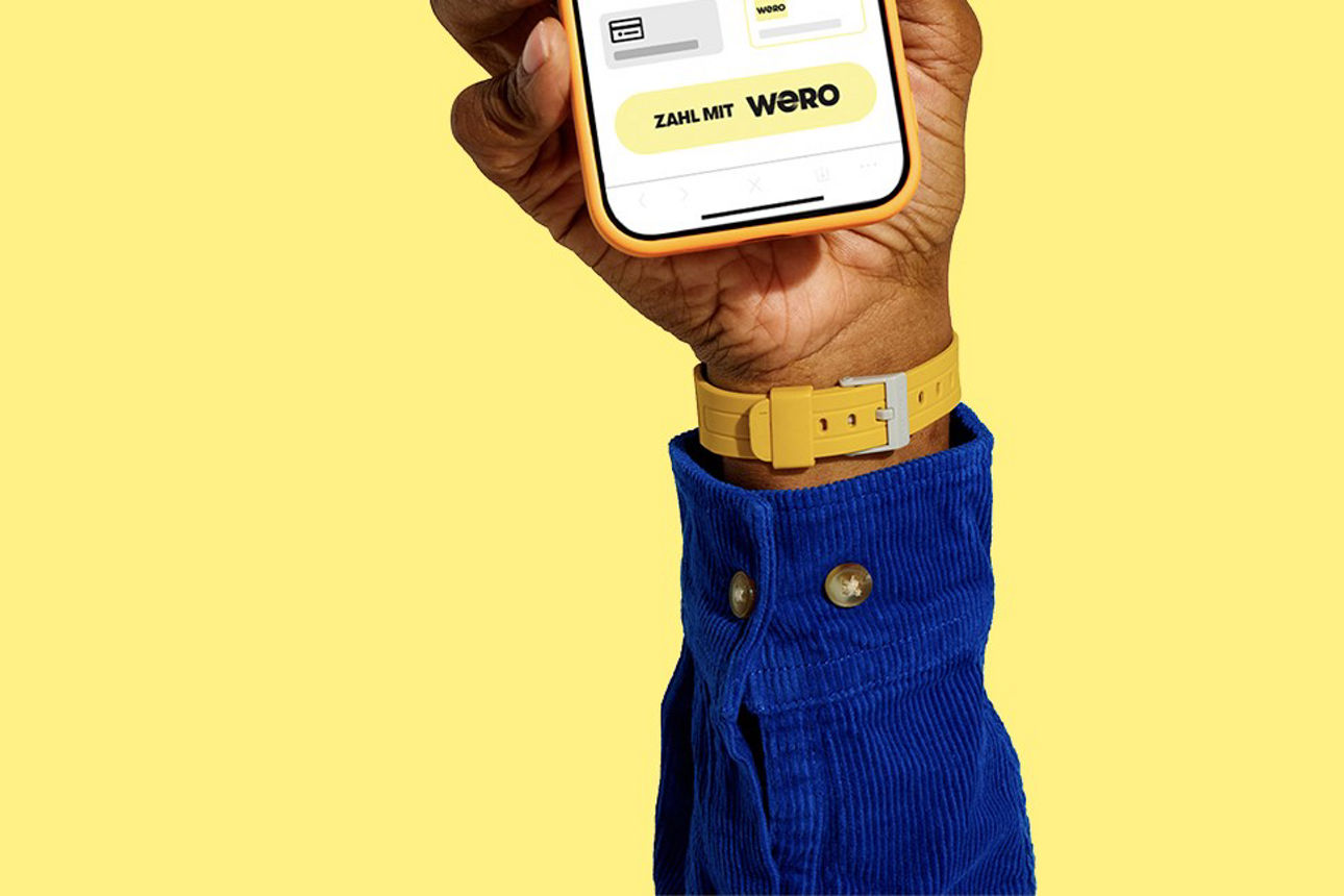 Eine Hand hält ein Handy hoch. Der Hintergrund ist gelb. 