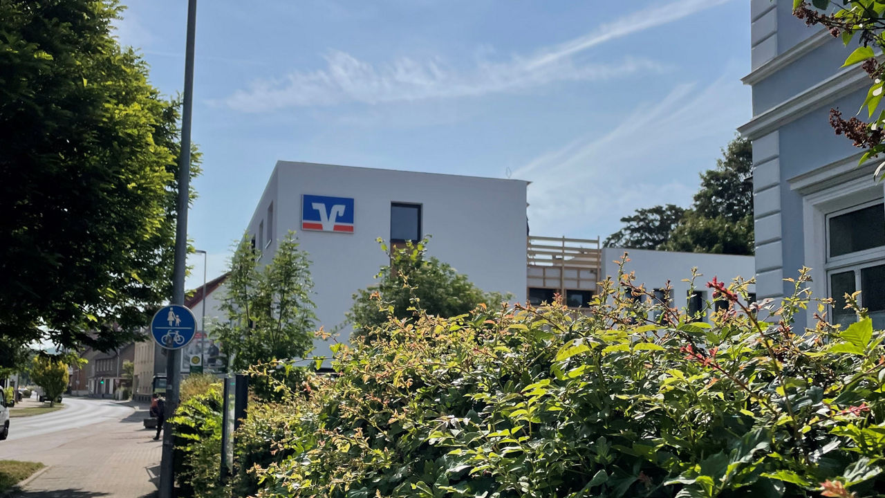 Unsere neue Filiale in Alfeld. Sie sehen das weiße Gebäude mit Flachdach und großem Volksbank Markenzeichen. 