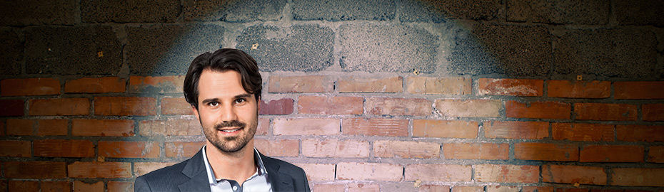 Ein professionelles Portraitfoto vor einem strukturierten Backsteinhintergrund.
