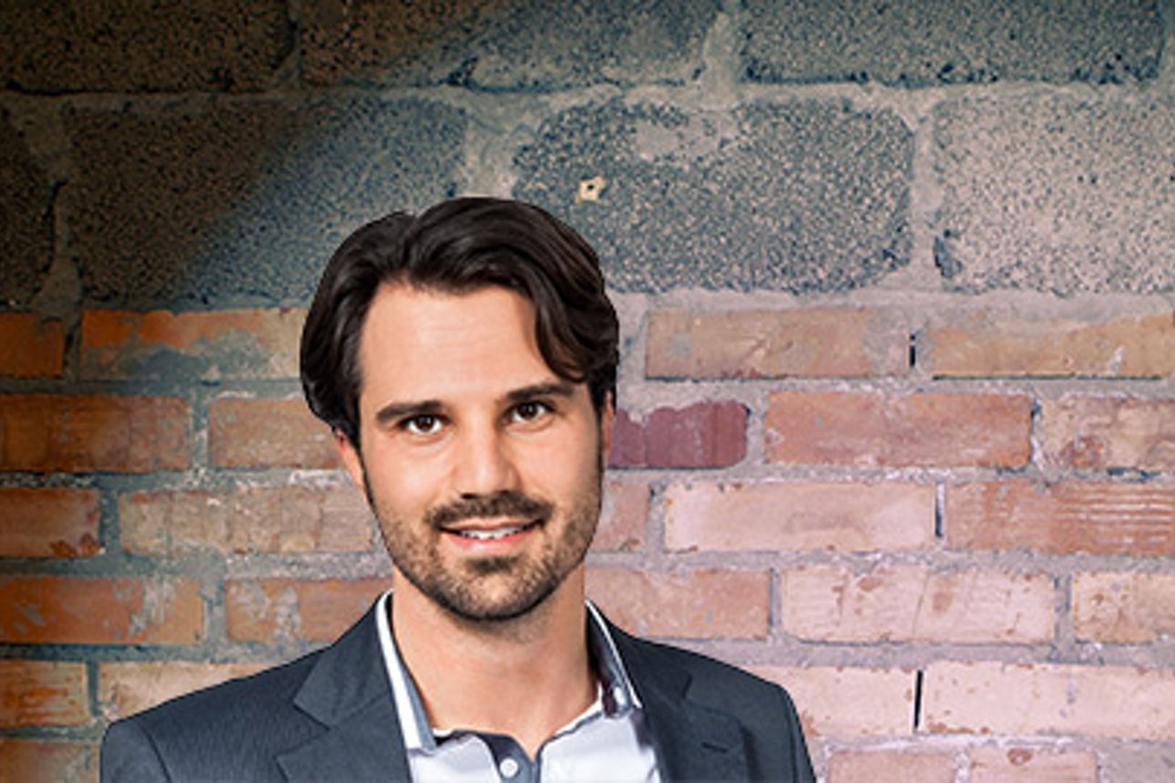 Ein professionelles Portraitfoto vor einem strukturierten Backsteinhintergrund.