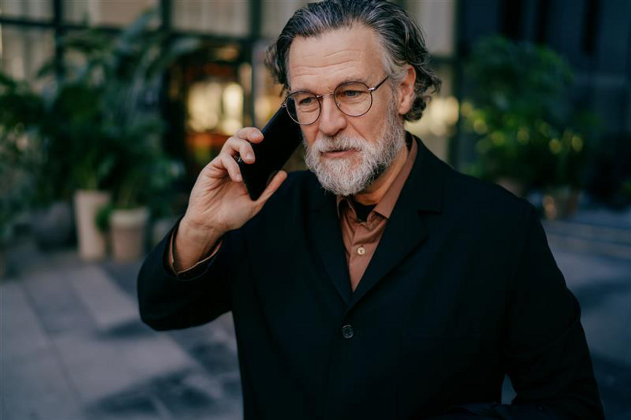 Eine Person hält ein Smartphone ans Ohr und telefoniert im Außenbereich eines modernen Gebäudes.