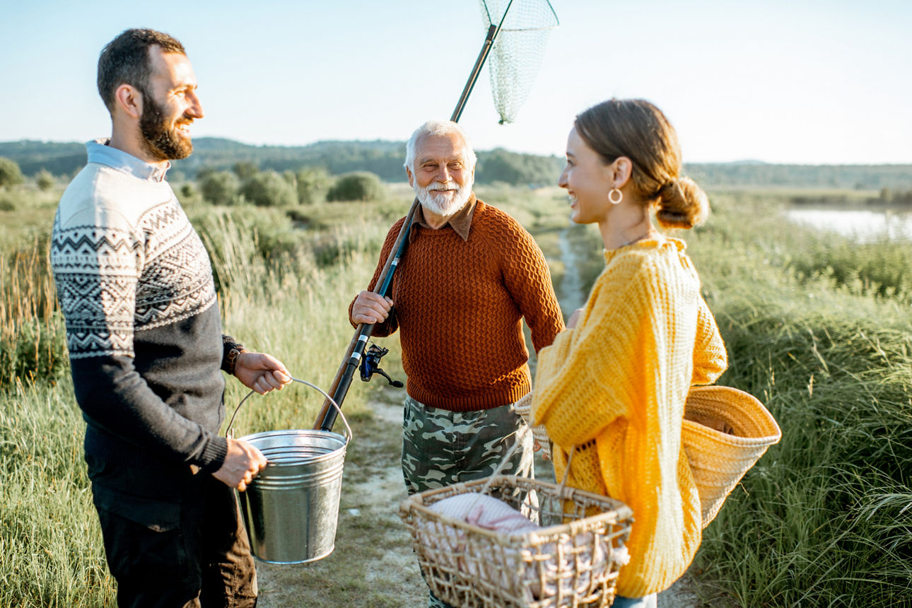 Young man and woman with senior grandfather dressed in sweaters spending a good time together while fishing in the morning