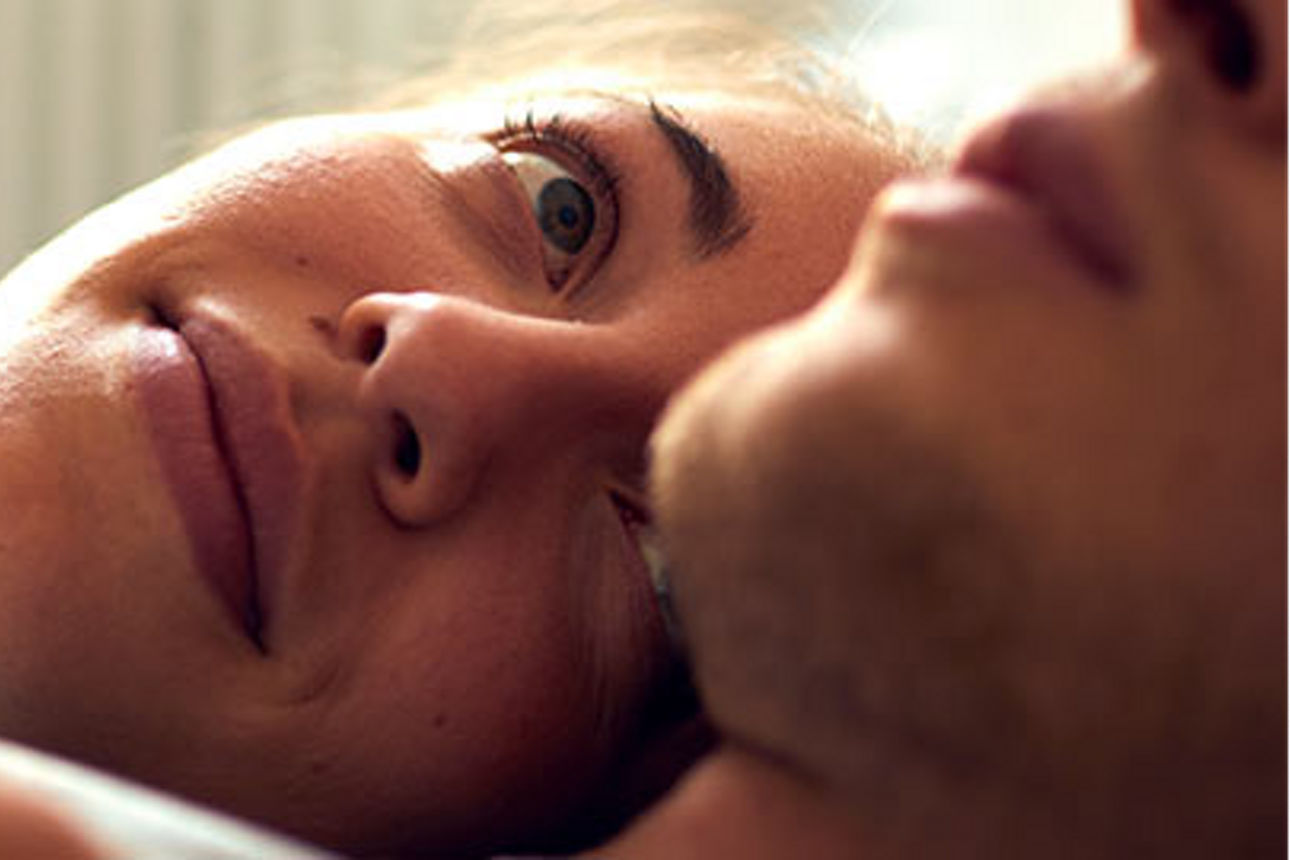 Ein Mann und eine Frau lächeln fröhlich, während sie zusammen im Bett liegen und eine warme und intime Atmosphäre schaffen.