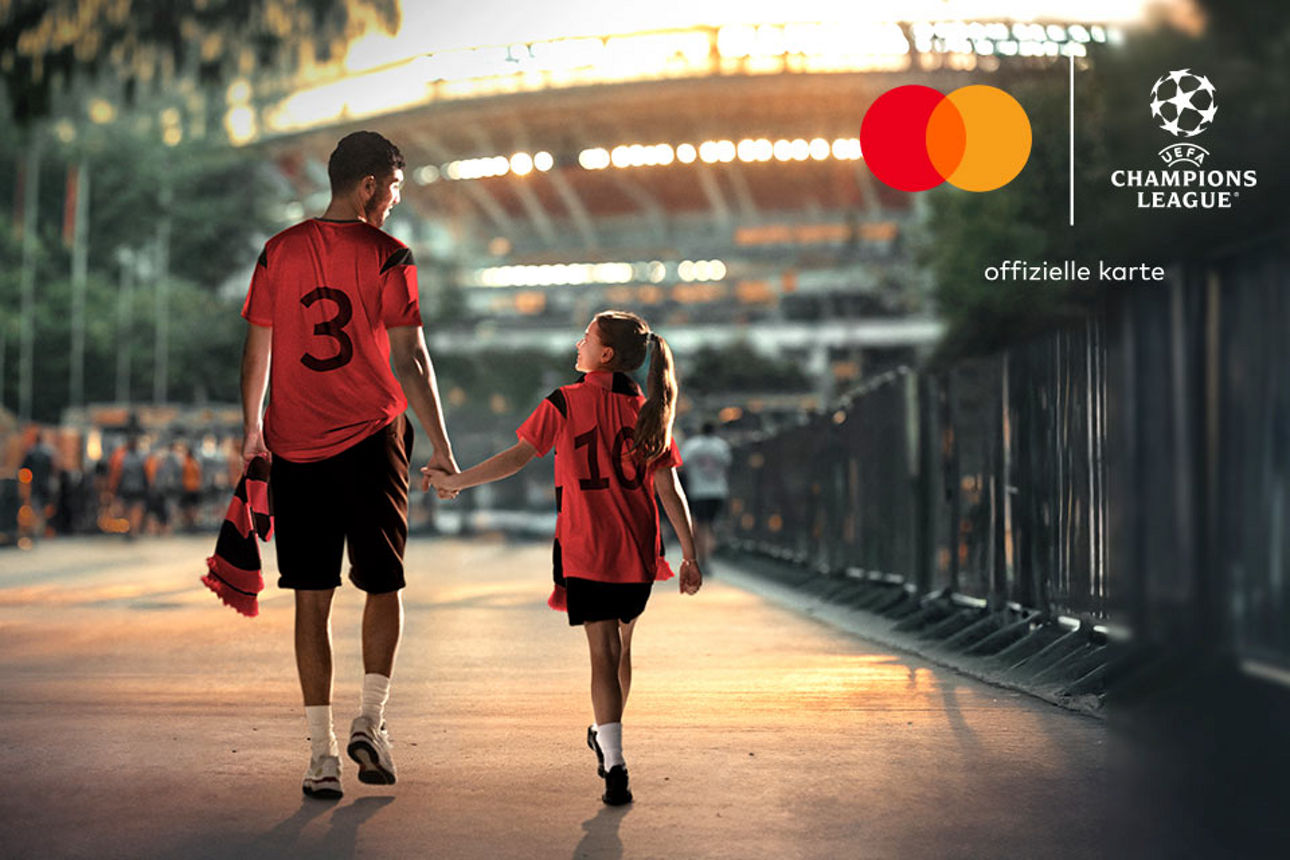 Ein Vater und sein Kind laufen Hand in Hand zum Stadion. Beide tragen Trikots und freuen sich auf das Spiel