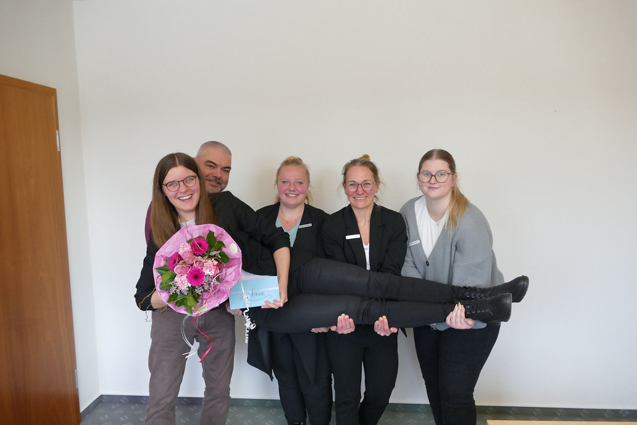 Junge Frau wird von ihren vier Kolleginnen gehalten, während alle lachen