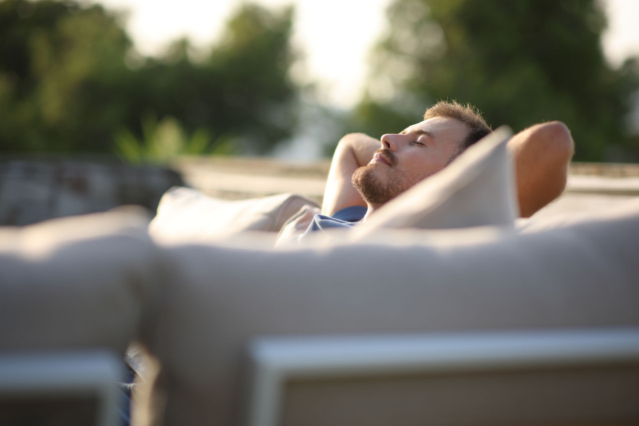 Mann liegt entspannt auf einem Outdoor-Sofa