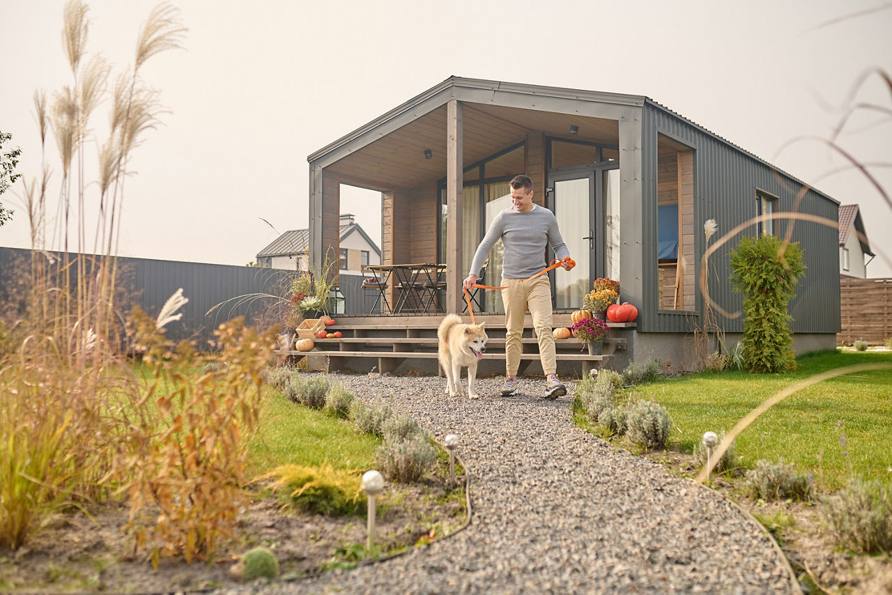 Ein Mann verlässt mit seinem weißen Hund das Haus über den Garten. 