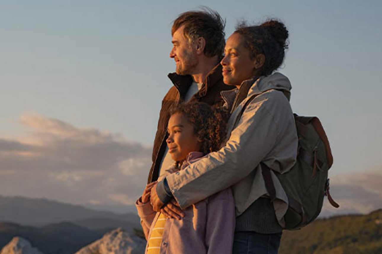 Eine Familie bei einer Wanderung in den Bergen schaut lächelnd dem Sonnenuntergang zu.