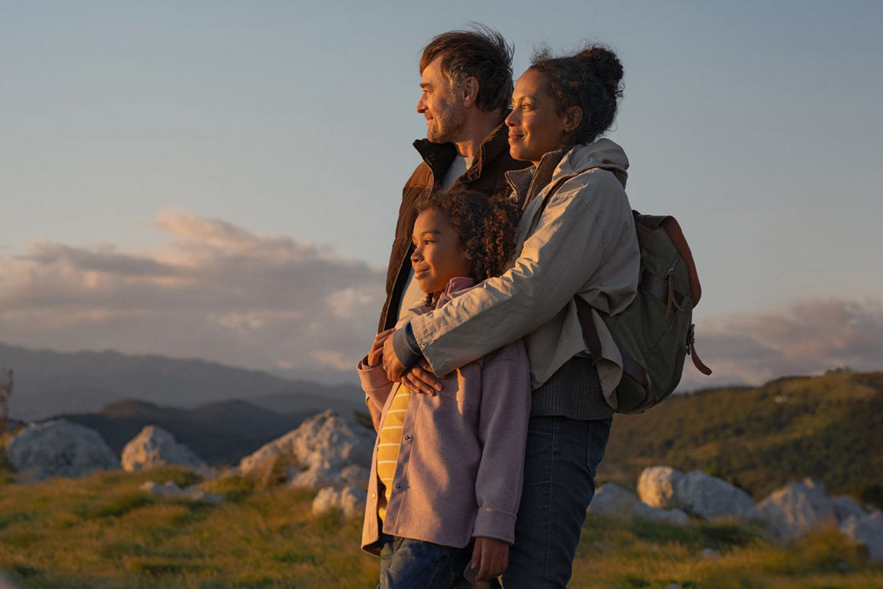 Mann sitzt am Tisch guckt auf einen Laptop lehnt sich zu rück und hat die Hände hinten am Kopf. 