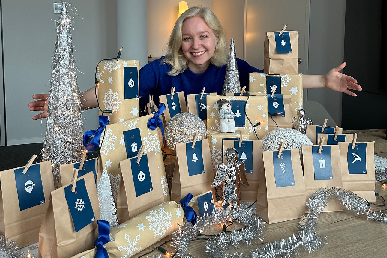 Eine junge Frau szeht hinter einem festlich geschmückten Adventskalender.