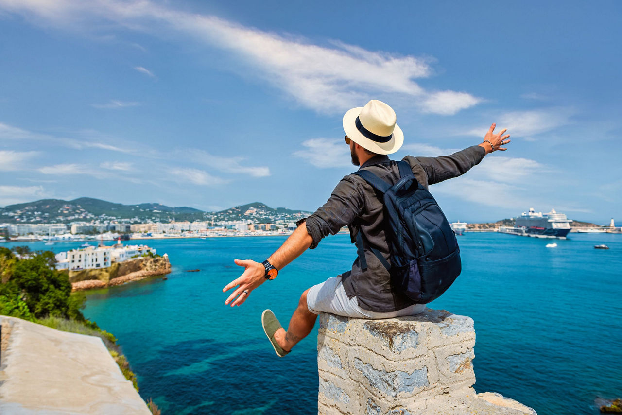 Ein Urlauber sitzt auf einer Mauer mit Blick auf das blaue Meer