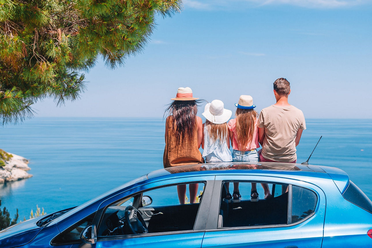 Eine vierköpfige Familie sitzt auf dem Autodach und schaut auf das offene Meer