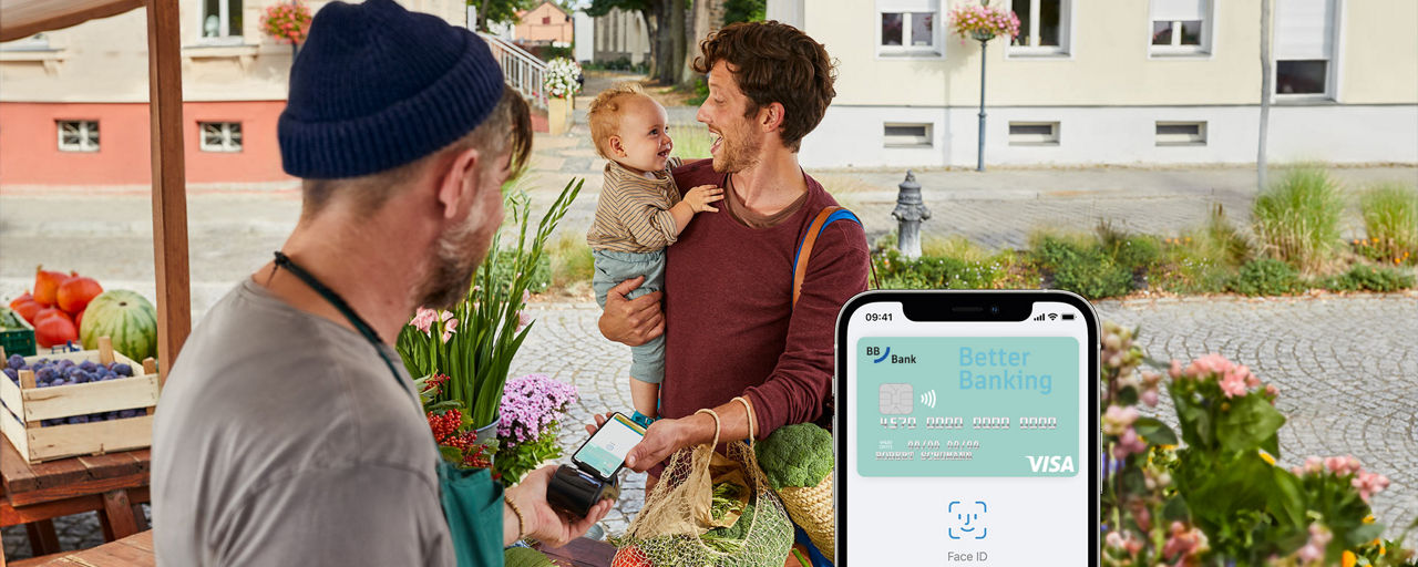Mann mit Baby im Arm bezahlt auf einem Markt mit Apple Pay.
