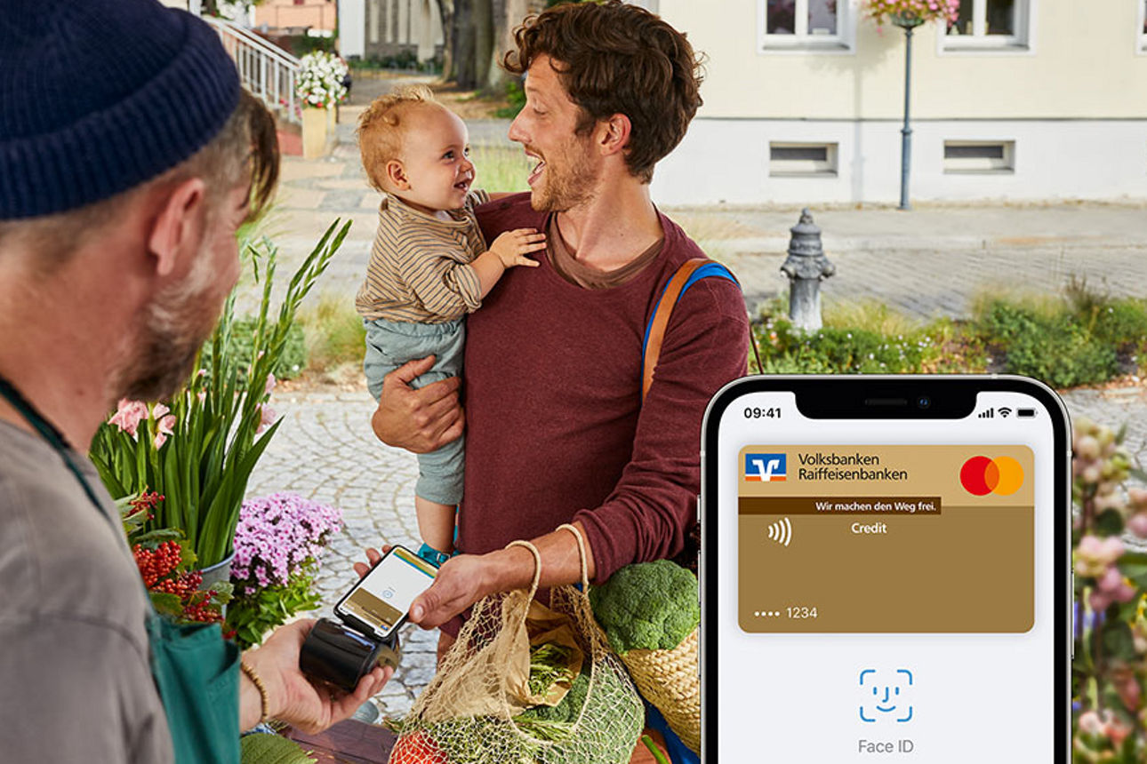 Mann mit Kind auf dem Arm bezahlt am Marktstand mit Apple Pay