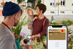 Vater mit Baby auf dem Arm zahlt auf dem Markt den Gemüseinkauf mit Apple Pay