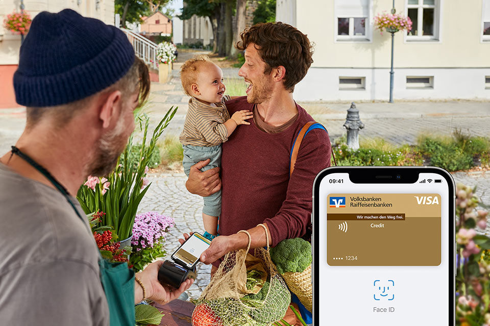 Mann mit Kind auf dem Arm bezahlt an Marktstand mit Apple Pay