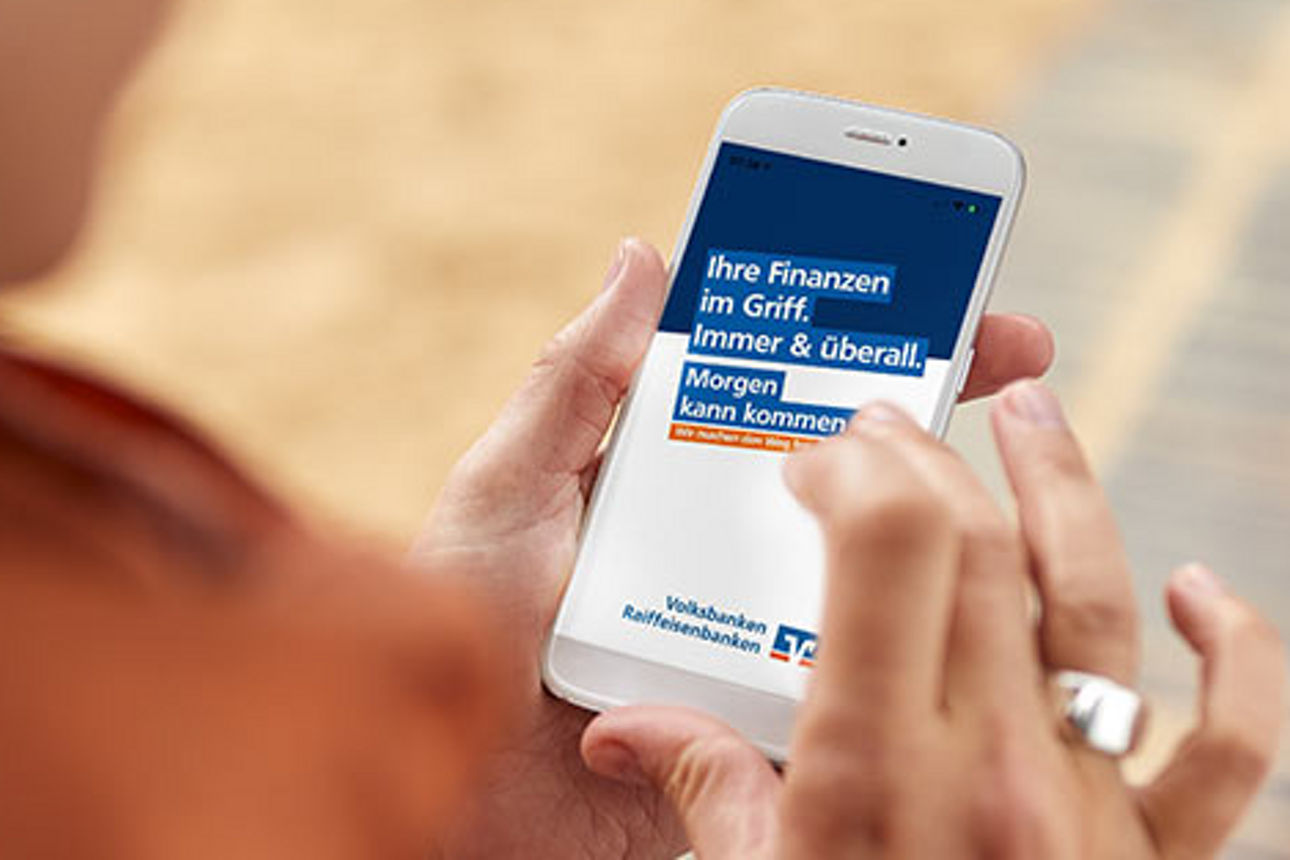 Jemand hält ein Smartphone in der Hand und schaut auf eine App der Volksbanken und Raiffeisenbanken